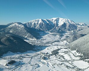 Schneebedecktes Alpen-Tal mit bewaldeten Bergen unter klarem blauen Himmel